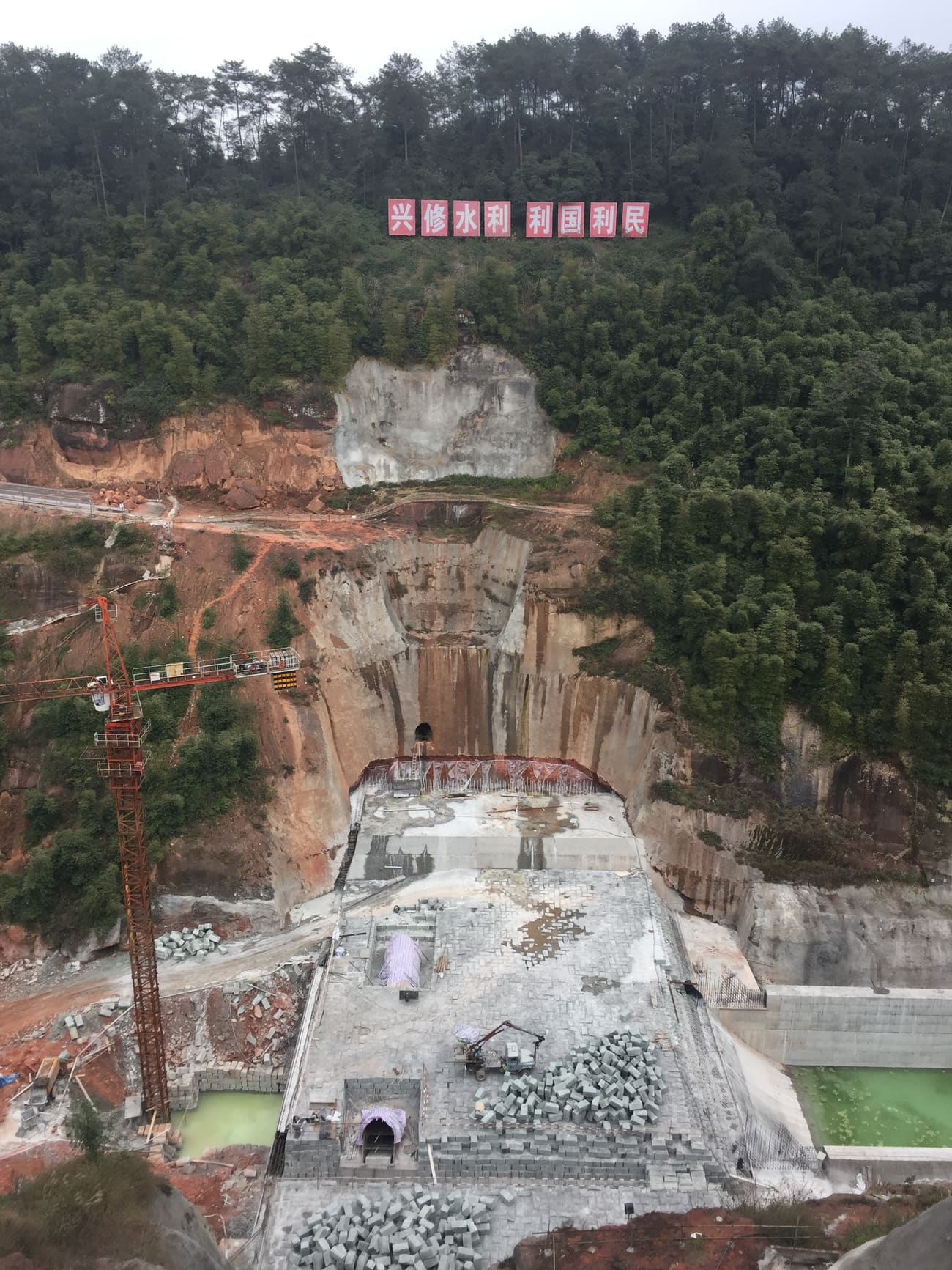 丘陵间在建的水库，标语写着“兴修水利 利国利民”